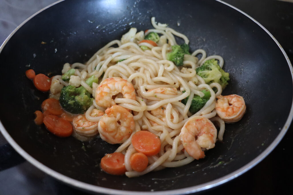 A pan of stir fried udon noodles with shrimp and veggies, combined with peanut lime vinaigrette