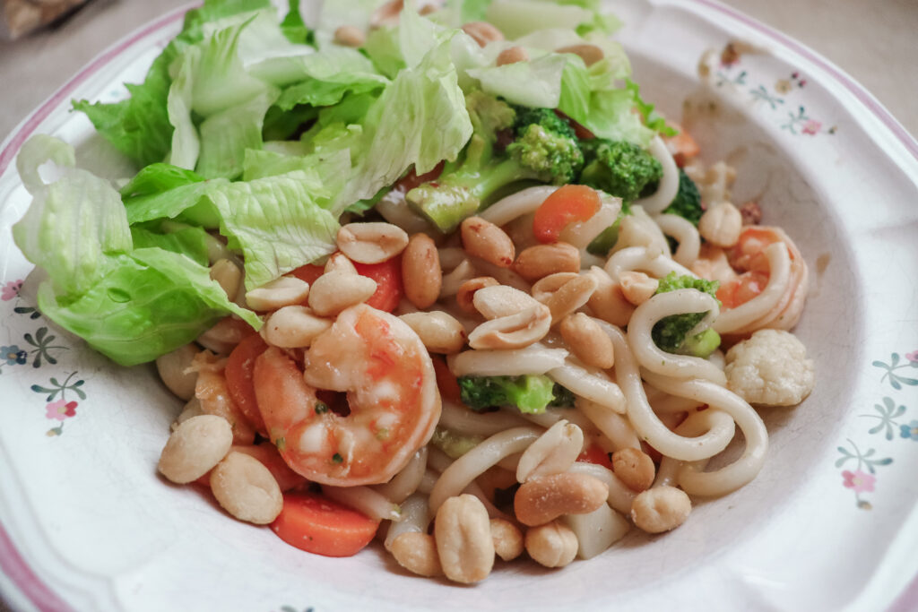 A bowl of stir fried udon noodles with shrimp, veggies, and fresh lettuce.